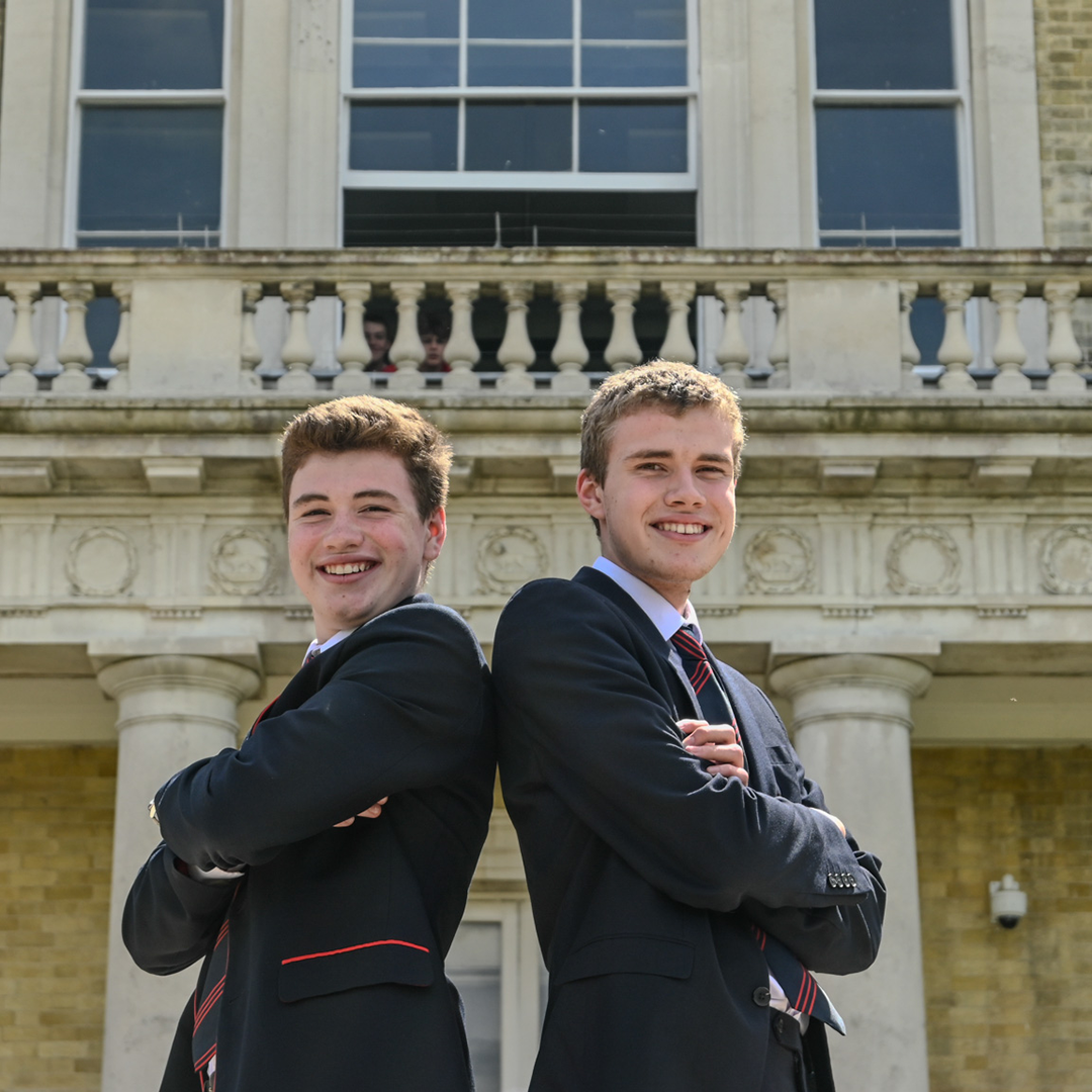 Two brothers posing back to back in front of main house at the City of London Freemen's School